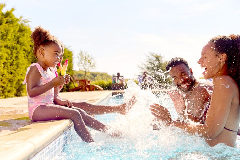 little girl sitting on the side of pool eating ice cream splashing parents