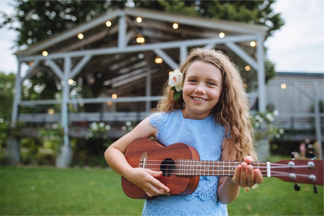 girl with flower in her ear playing a ukelele outdoors