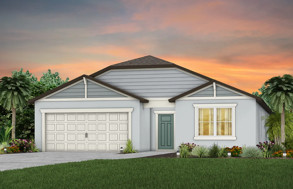 A single-story light blue house with white trim, a two-car garage, and a front door centered under a peaked roof, surrounded by green grass, palm trees, and colorful plants at sunset.