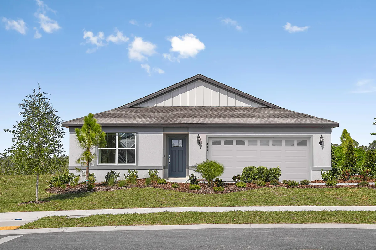 A single-story modern house with a gray roof, white exterior, a front lawn with shrubs, a dark front door, and a two-car garage, set against a blue sky with a few clouds.