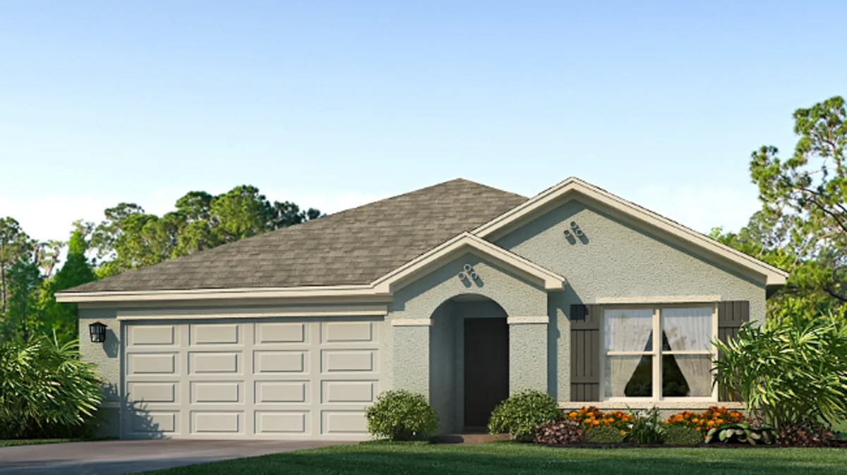 A single-story house with a double garage, light gray exterior, pitched roof, arched entryway, large front window, and landscaped yard with shrubs and colorful flowers. Trees are visible in the background under a clear sky.