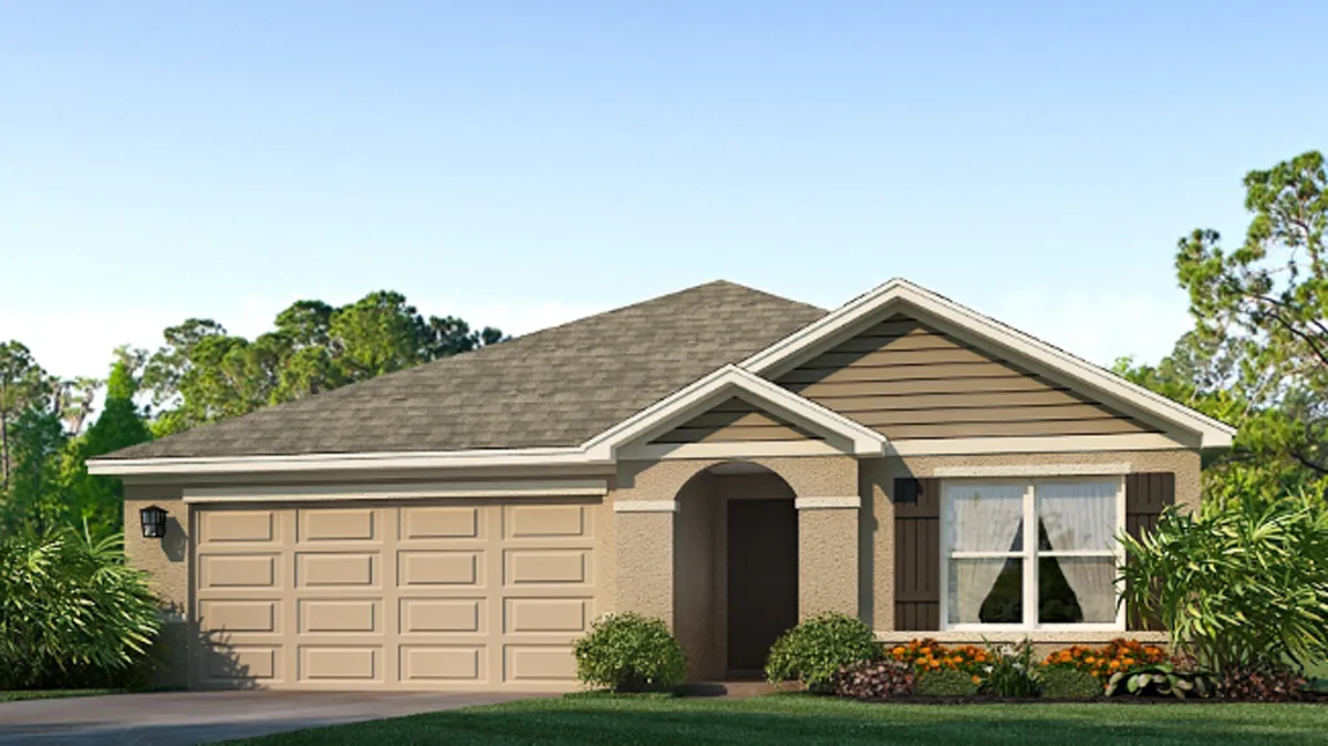 Single-story suburban house with a two-car garage, tan exterior, gabled roof, and a small arched entryway. There are bushes and flowers in front, with trees and blue sky in the background.