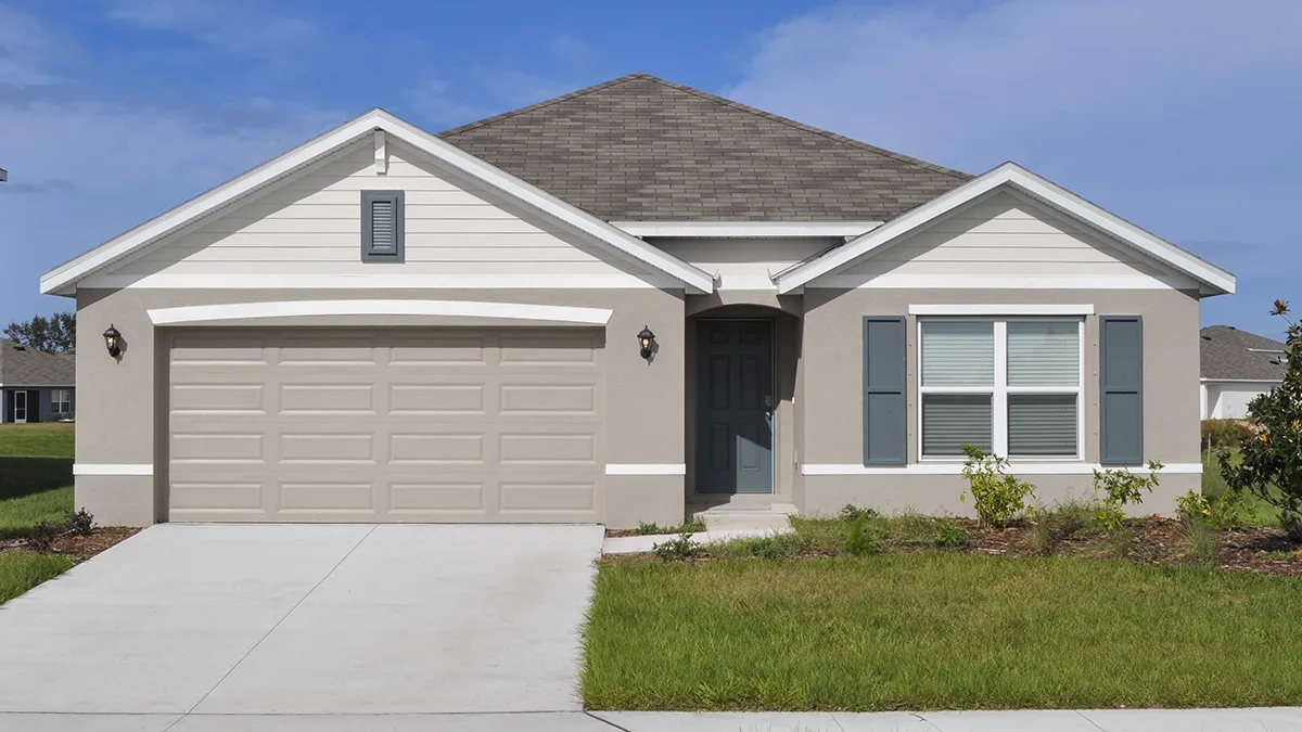 Single-story suburban house with light gray siding, a two-car garage, a front porch, and blue-gray shutters. The home has a neatly trimmed lawn and a clear blue sky in the background.