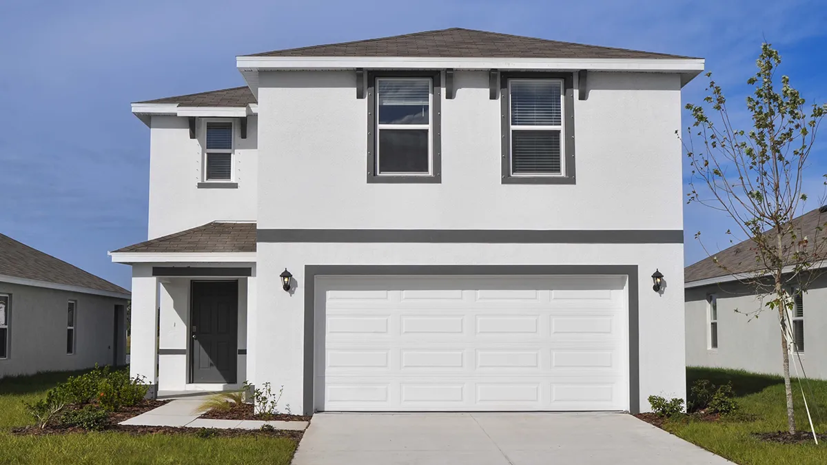 A modern two-story white house with a gray roof, a double garage, and a small front porch. It has two upper front windows and simple landscaping with green grass and small plants along the walkway.
