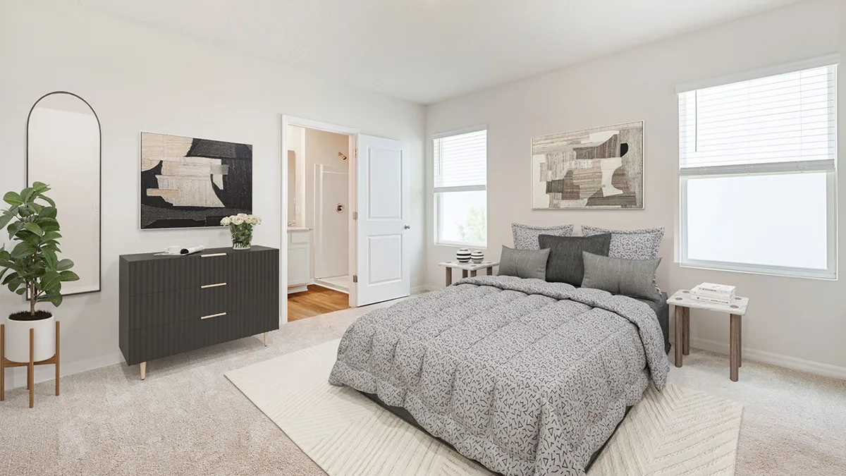 A modern bedroom with a neatly made bed, gray patterned bedding, a dark dresser with a plant, abstract artwork on white walls, two windows, and an open door showing a glimpse of a bathroom.