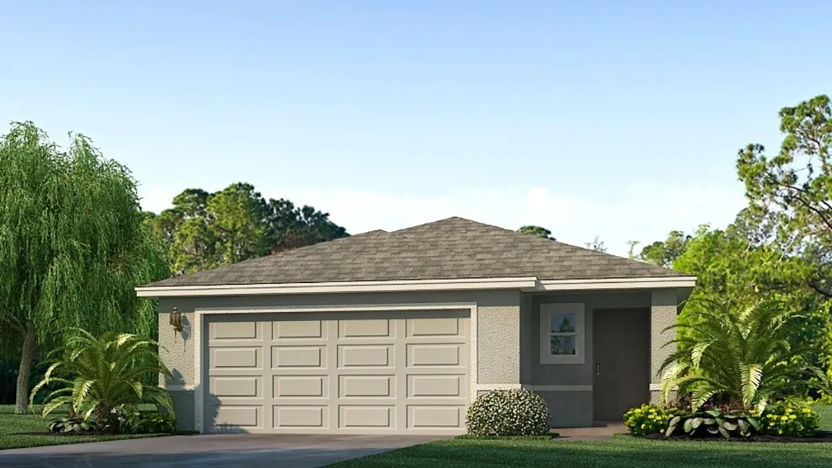 A single-story house with light gray walls, a double garage door, a short driveway, and simple landscaping with shrubs and palm plants in front. The sky is clear and trees are visible in the background.