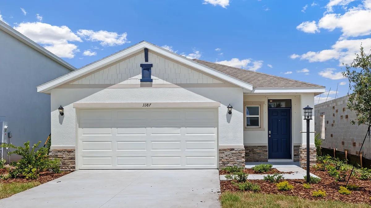 A modern single-story house with a white exterior, stone accents, a double garage, blue front door, and small front yard landscaping, under a blue sky with scattered clouds.