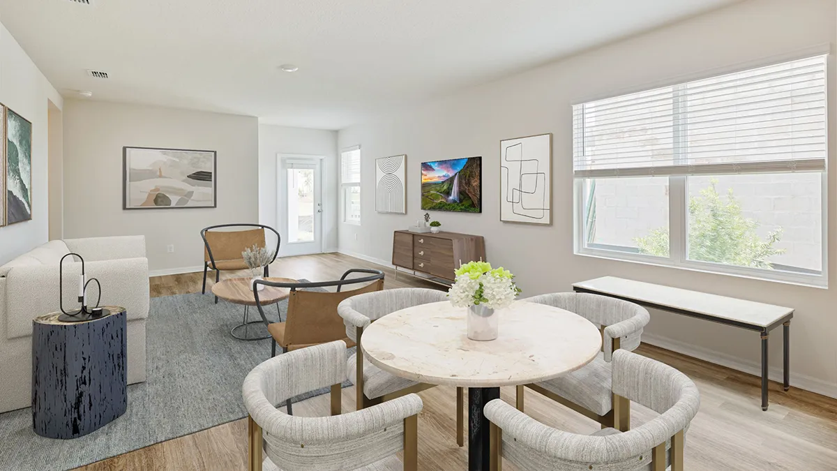 Modern living and dining area with light walls, wooden flooring, round marble dining table with four chairs, two armchairs, a sofa, TV on a wooden console, large window, wall art, and indoor plants.
