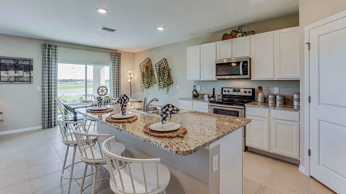 Modern kitchen with light cabinets, granite countertops, stainless steel appliances, and a breakfast bar set with four place settings; large windows provide natural light and a view outside.