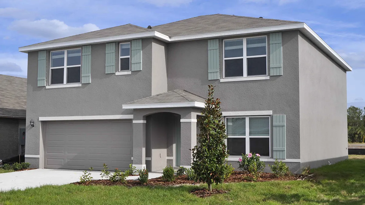 A two-story modern suburban house with light gray exterior walls, green window shutters, a two-car garage, and a small covered entryway, surrounded by a grassy lawn and young landscaping.