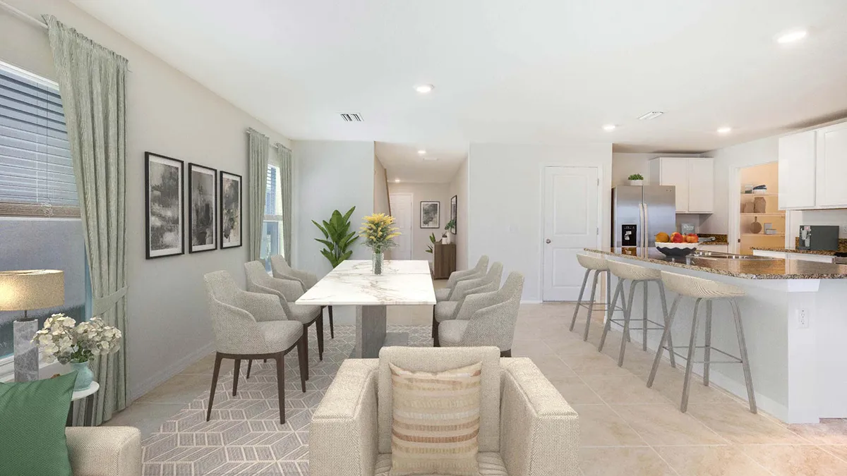 Open-concept dining and kitchen area with a marble dining table, eight upholstered chairs, breakfast bar with stools, stainless steel appliances, neutral decor, and large windows with sheer curtains.