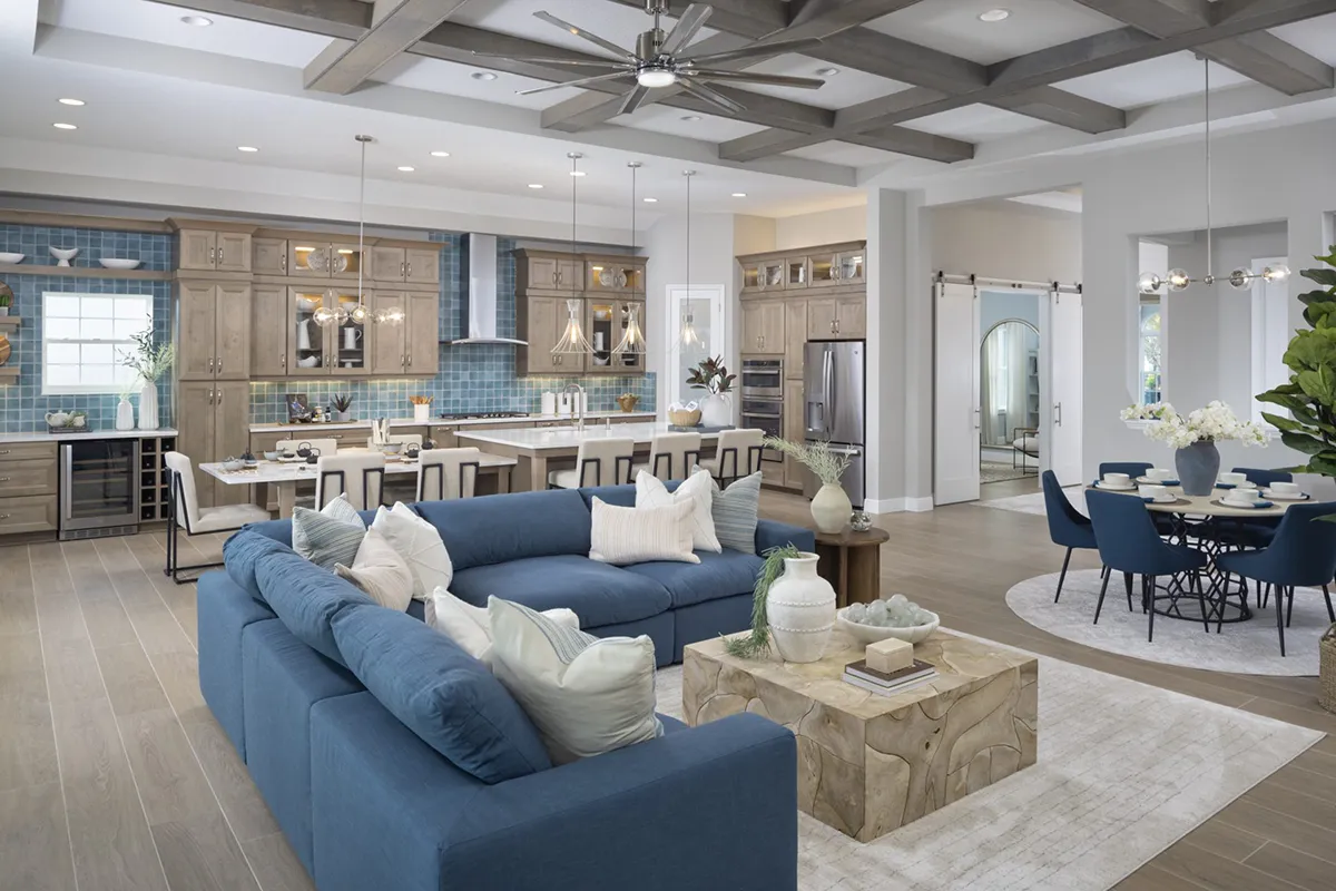 Spacious open-concept living area with a blue sectional sofa, wooden coffee table, modern kitchen with bar stools, and a round dining table; neutral tones and stylish decor throughout.