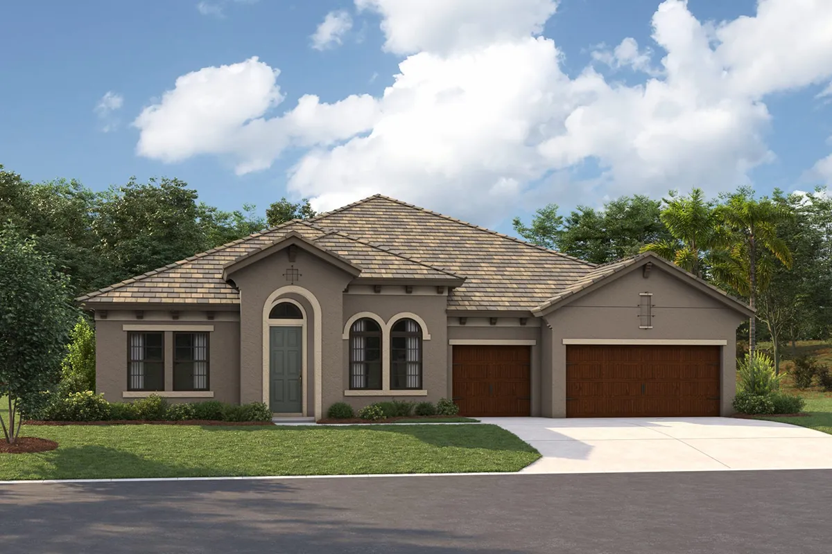 Single-story suburban house with a tan exterior, arched windows, and a gray front door. The home has a three-car garage with wooden doors, a manicured lawn, and trees in the background under a partly cloudy sky.
