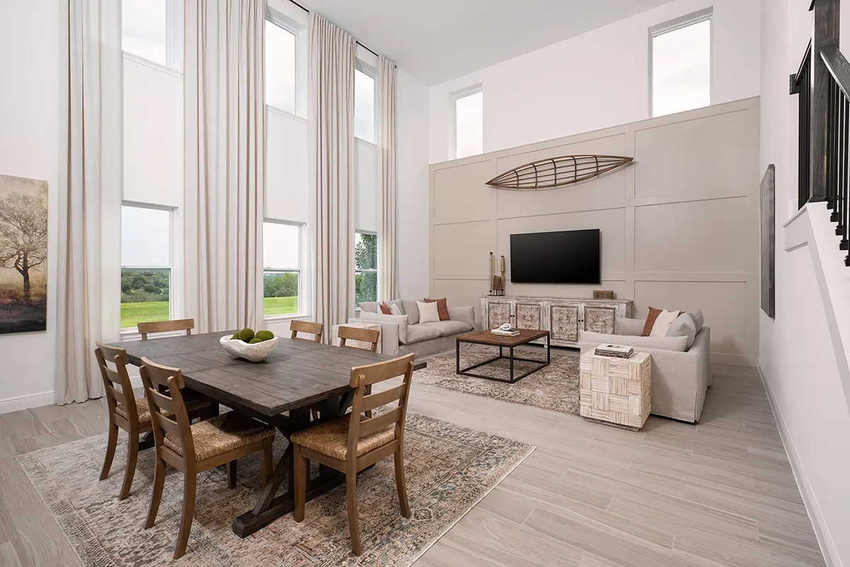 Modern living and dining area with high ceilings, tall windows with white curtains, a dark wooden dining table with chairs, two light sofas, a TV mounted on the wall, and neutral decor with natural light filling the space.
