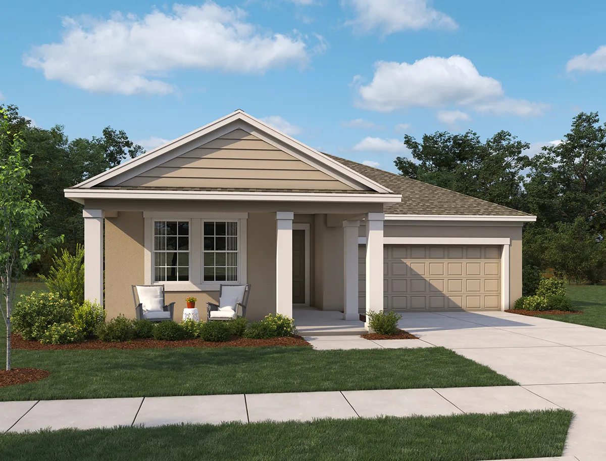 A single-story beige house with a covered front porch, two chairs and a small table, attached two-car garage, landscaped yard, and a driveway, set against a backdrop of trees and a blue sky with clouds.