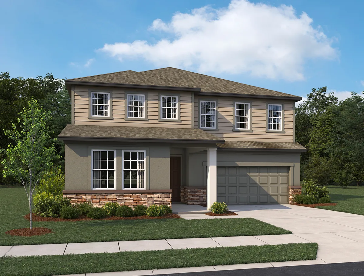 Two-story suburban house with tan siding, gray garage door, stone accents, and front porch. Manicured lawn, small shrubs, and a young tree in the front yard. Blue sky with scattered clouds and trees in the background.