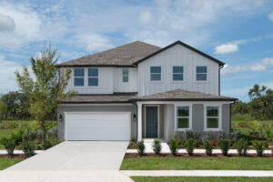A modern two-story house with white siding and gray accents, featuring a two-car garage, a covered front porch, and a manicured front yard with bushes and a small tree, set against a blue sky with scattered clouds.